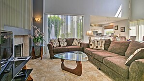 A spacious living room with a glass coffee table, two sofas with patterned cushions, a fireplace, and a view of the outdoors through large windows. - Elegant and spacious two-story suite near Palm Springs (Cathedral City)