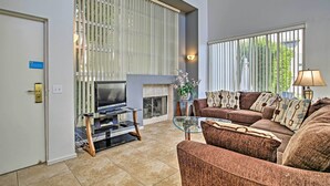 A modern living room with a fireplace, a sofa set, a TV on a stand, and a glass coffee table. - Elegant and spacious two-story suite near Palm Springs (Cathedral City)