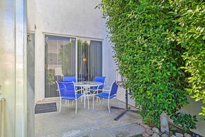 A patio with a table and blue chairs, a sliding glass door, and a green hedge. - Elegant and spacious two-story suite near Palm Springs (Cathedral City)