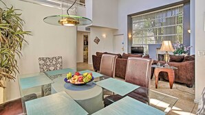 A modern living room with a glass dining table, brown leather sofas, and a large window with blinds. - Elegant and spacious two-story suite near Palm Springs (Cathedral City)