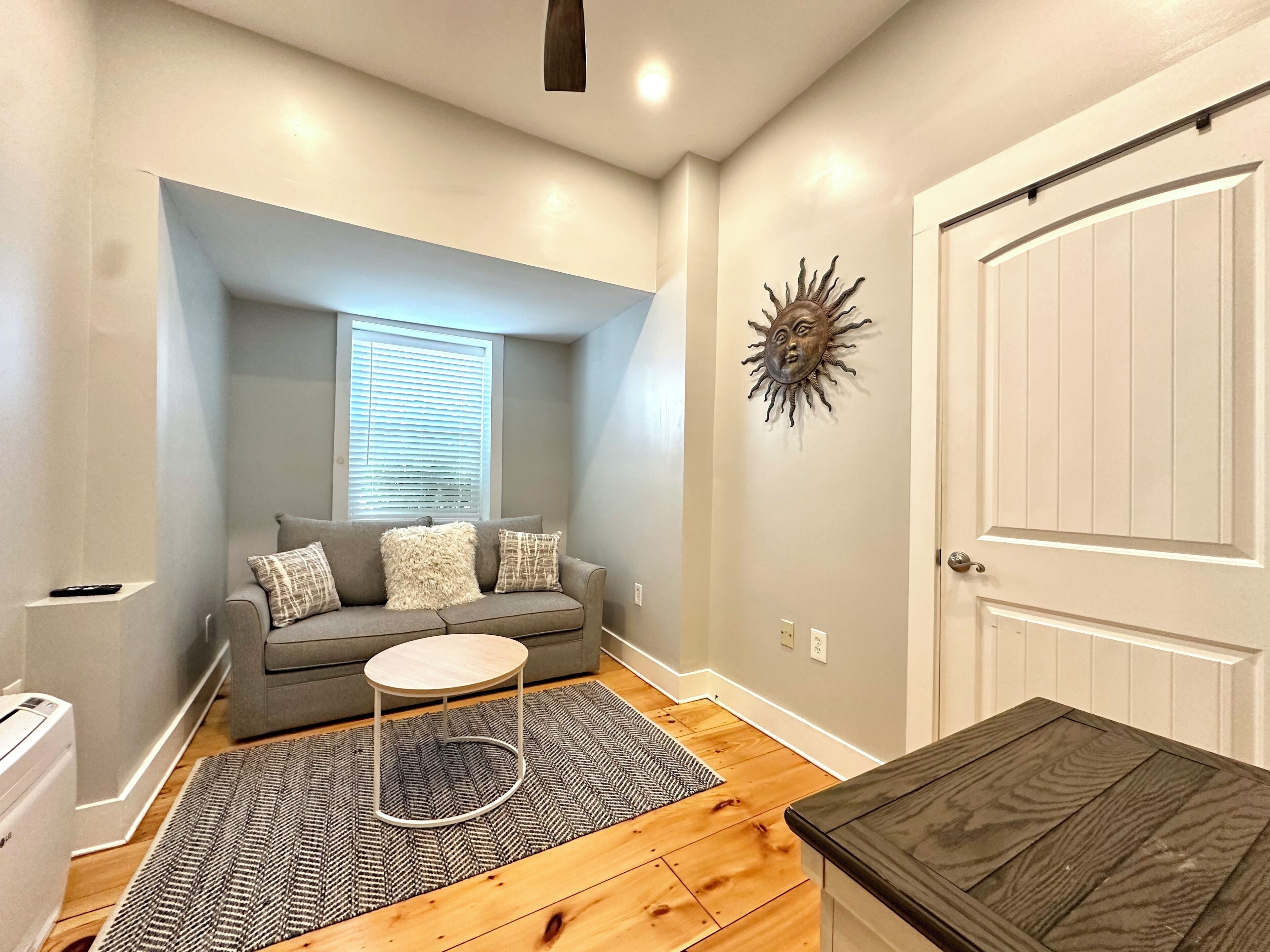 A living room with a gray sofa, a small round table, a patterned rug, and a wooden floor.