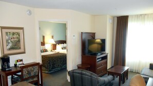 A hotel room with a bed, a TV, a coffee maker, and a seating area with a couch and chairs.