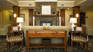 A hotel lobby with a stone fireplace, two armchairs, a wooden console table, and a patterned carpet.