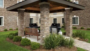 A covered patio with stone pillars, outdoor grills, and a bench.