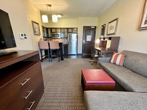 A compact living space with a sofa, a television, a kitchenette, and a dining area. - Suite 4-Mins from Airport | Fitness Center + Pool (Carlsbad)