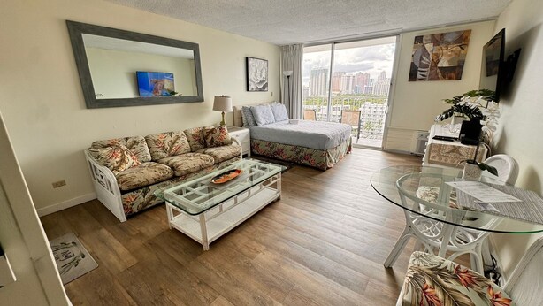 A living room with a sofa, a glass coffee table, a dining table with chairs, a large window with a city view, and a mirror on the wall. - 8 GUESTS, 2 X ❤️AWESOME STUDIOS❤️ FREE PARKING, 5MIN TO OCEAN (Honolulu)