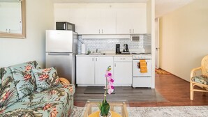 A compact kitchen with white cabinets, a refrigerator, and a stove. There is a dining area with a floral sofa and a small table with a vase of flowers. - 8 GUESTS, 2 X ❤️AWESOME STUDIOS❤️ FREE PARKING, 5MIN TO OCEAN (Honolulu)