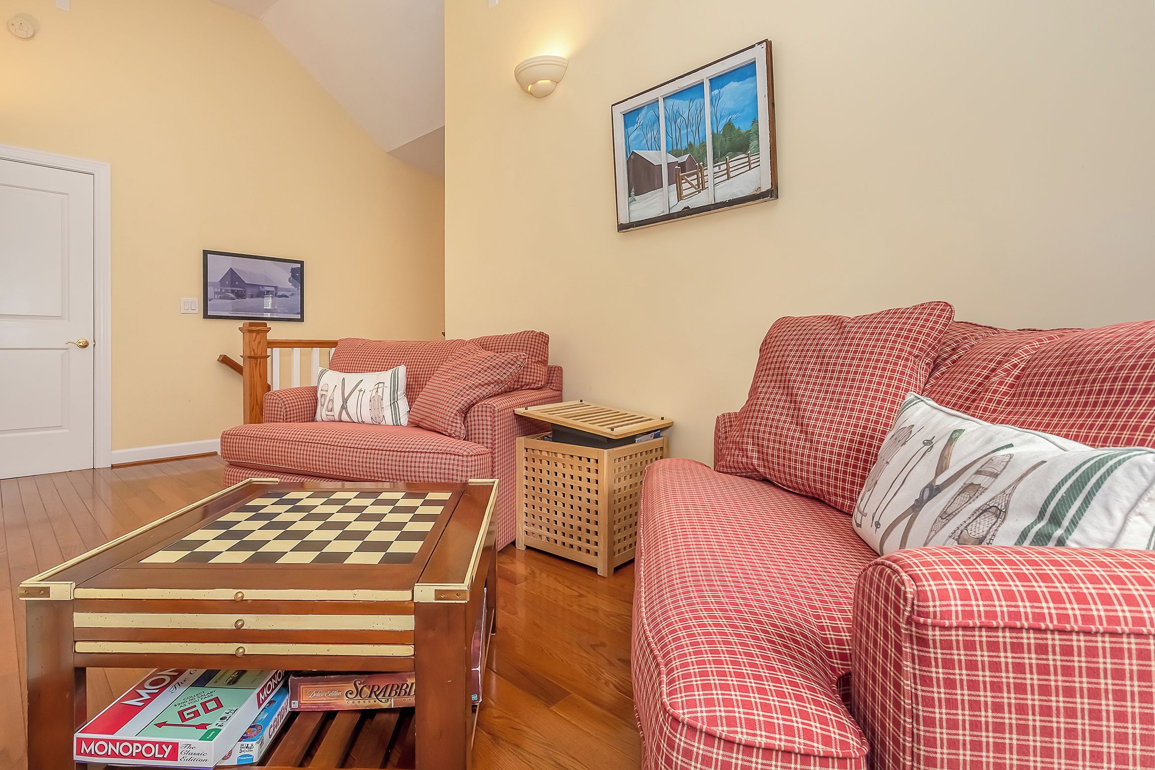 Ein gemütliches Wohnzimmer mit einer gepolsterten Couch in Karomuster, einem Couchtisch aus Holz mit einem Schachbrett und einem gerahmten Bild an der Wand.