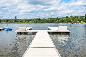 A wooden dock extending into calm water with two white benches and a small boat.