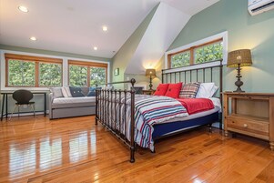 Un dormitorio con cama, escritorio, silla y ventanas amplias.