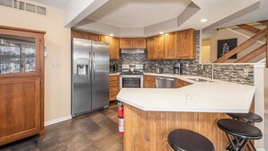 Une cuisine moderne dotée d’un réfrigérateur en acier inoxydable, de meubles en bois, d’un four encastré et d’un grand îlot central avec des tabourets de bar.