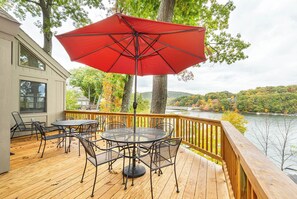 Une terrasse en bois avec des meubles d’extérieur, un parasol rouge et une vue sur un lac et des arbres.