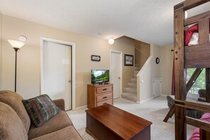 A living room with a sofa, a coffee table, a TV on a wooden stand, a staircase, and a door labeled "LAKE". - 180 Degrees by Taylor Made Deep Creek (Oakland)