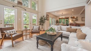 A spacious living room with a large window, a dining area, and a kitchen visible through an open door. - Sunset Pointe by Taylor Made Deep Creek (Oakland)