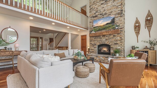 A spacious living room with a stone fireplace, a high ceiling, and a view of the outdoors. - Sunset Pointe by Taylor Made Deep Creek (Oakland)