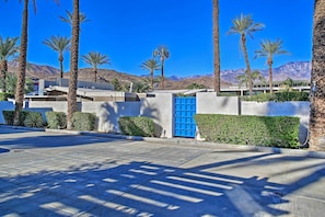 A paved driveway leading to a building with a blue door, surrounded by palm trees and a mountainous backdrop. - Gorgeous and spacious (Cathedral City)