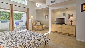 A bedroom with a bed, a TV, a dresser, and a seating area with a chair and a sofa.