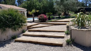 A garden with a pool, palm trees, and a wooden staircase leading to a building. - Studio Le soleil couchant, in Provence near Avignon (Saint-Saturnin-lès-Avignon)