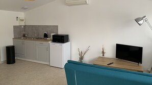 A compact living space with a kitchenette, a dining area with a TV and remote, a sofa, and a lamp. - Studio Le soleil couchant, in Provence near Avignon (Saint-Saturnin-lès-Avignon)
