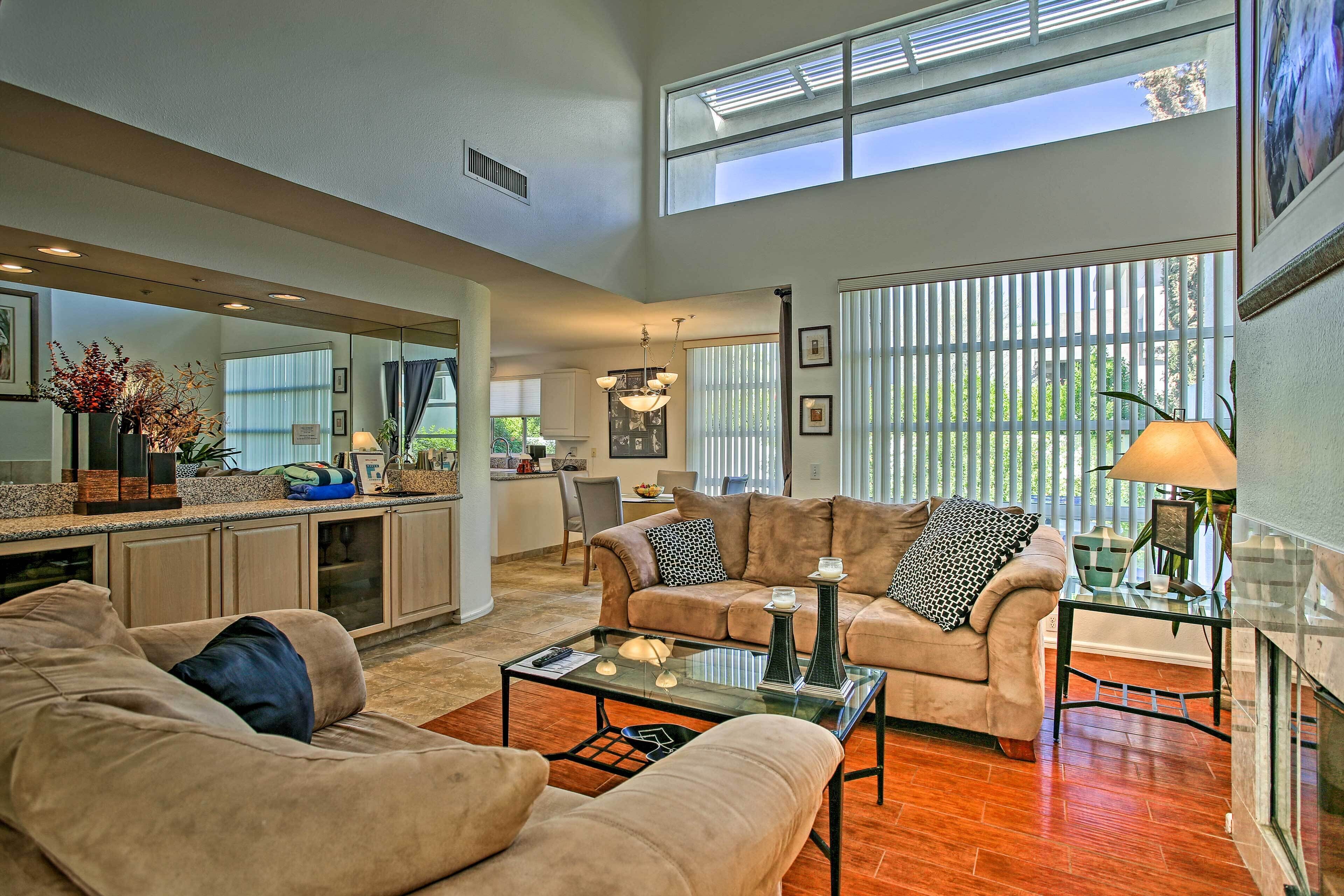A spacious living area with a large window, a kitchen in the background, and a cozy seating arrangement.