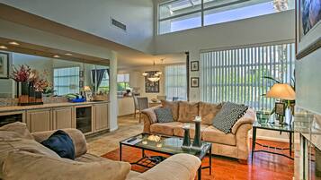 A spacious living area with a large window, a kitchen in the background, and a cozy seating arrangement.
