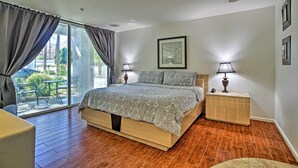 Un dormitorio con piso de madera, una cama con cubrecama estampado, dos lámparas de noche, una mesita de noche y un ventanal con cortinas.
