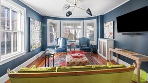 A living room with a large window, a ceiling fan, a TV, and a green sofa. - Chart House Inn (Newport)