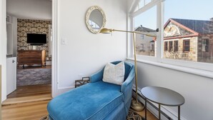 A room with a blue sofa, a round mirror, a floor lamp, a small table, and a window with a view of buildings. - Chart House Inn (Newport)