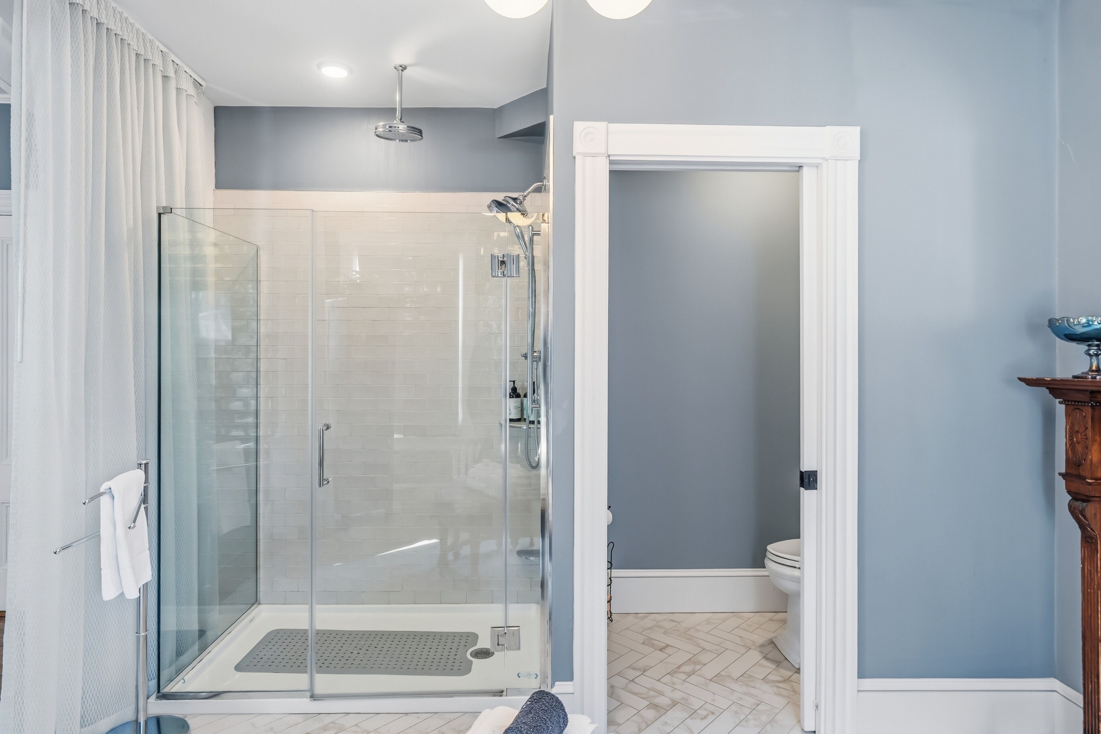 A modern bathroom with a glass shower enclosure, a white toilet, and a wooden pedestal sink.
