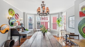 A dining area with a wooden table, chairs, a chandelier, and artwork on the walls. - Chart House Inn (Newport)