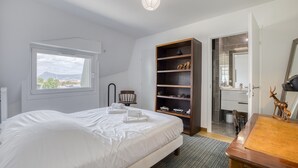 Un dormitorio con cama, una estantería de madera, un escritorio y un baño visible a través de una puerta abierta.