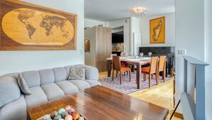 Una sala moderna con sofá, mesa de centro de madera, comedor con sillas, un mapa del mundo en la pared y una cocina al fondo.