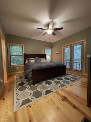 A bedroom with a bed, a ceiling fan, and large windows.