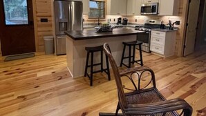 Eine geräumige Küche mit Holzböden, einer zentralen Kochinsel mit Sitzgelegenheiten, einem Kühlschrank und einer Mikrowelle.