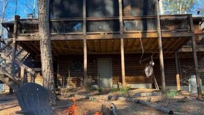 Eine Holzhütte mit Feuerstelle davor, umgeben von Bäumen.