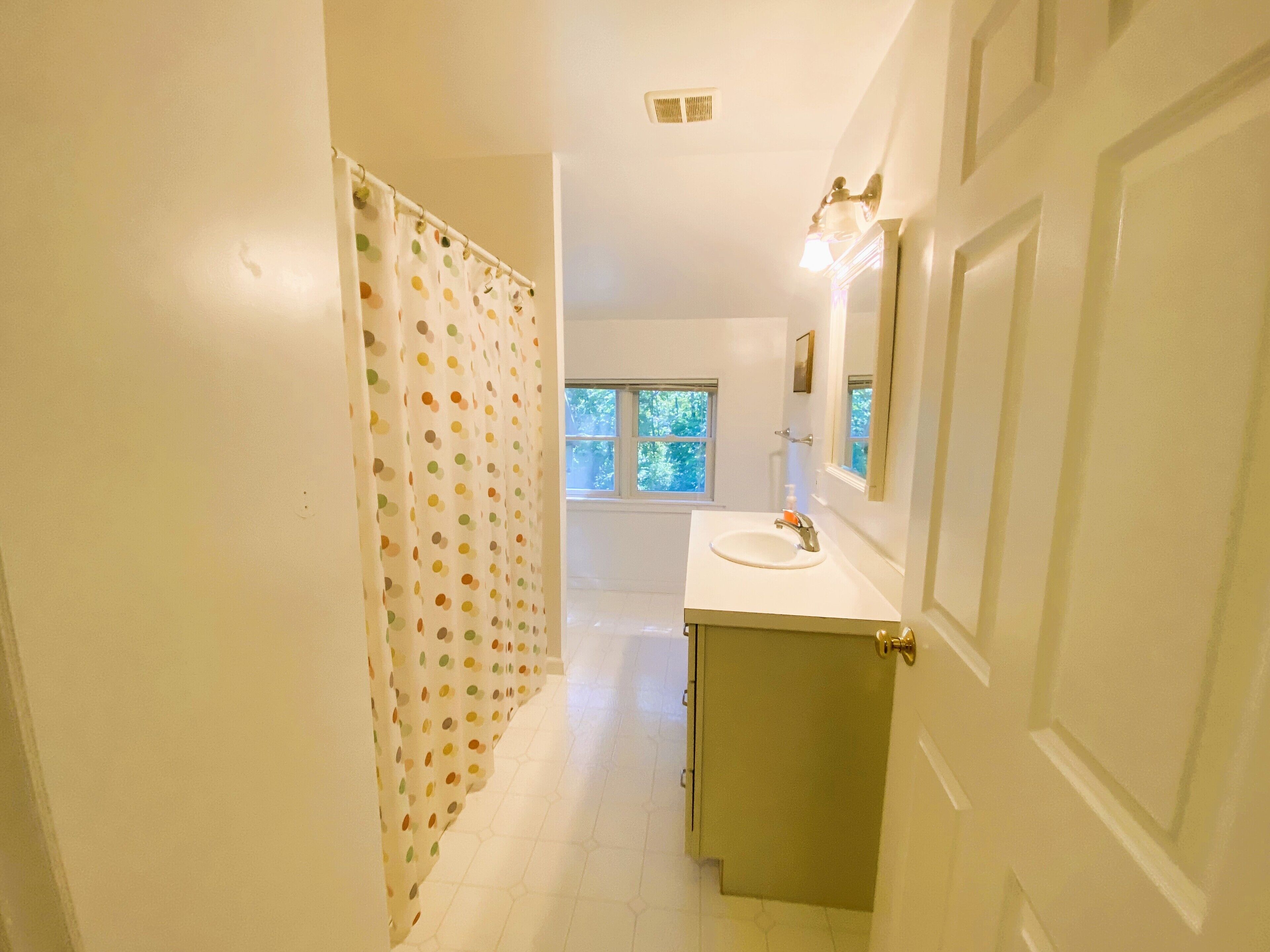A narrow hallway leading to a bathroom with a white sink, a mirror, and a shower curtain with a polka dot pattern.