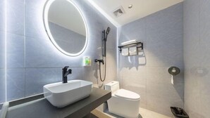 Une salle de bain moderne avec un grand miroir ovale, un lavabo sur colonne, des toilettes et un espace douche.