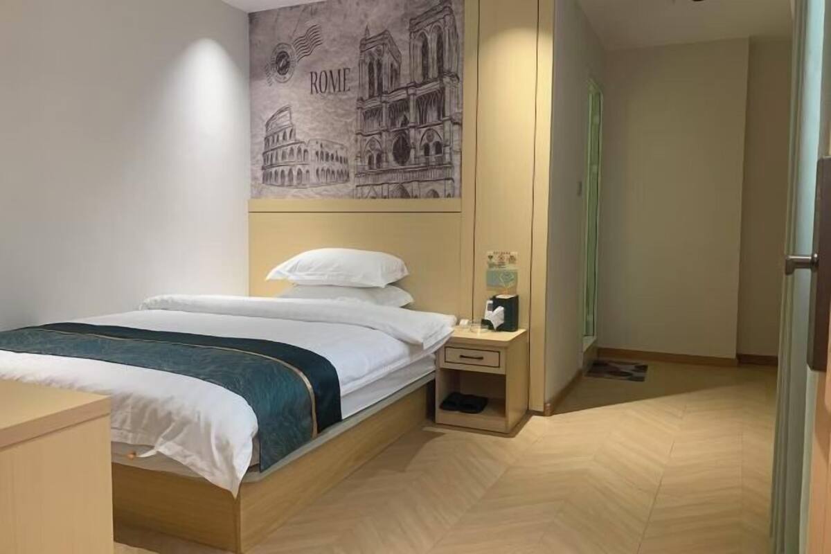 A neatly arranged bedroom with a bed, a nightstand, and a wall-mounted artwork depicting famous Roman architecture.