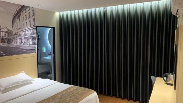 Une chambre d’hôtel équipée d’un lit, d’un bureau, d’un miroir, d’un rideau et d’un climatiseur fixé au mur.