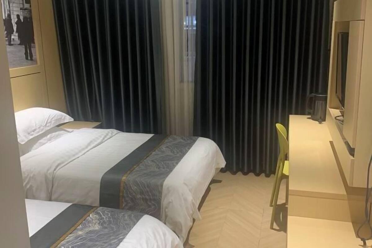 A hotel room with two beds, a desk with a chair, a TV, and a window with curtains.