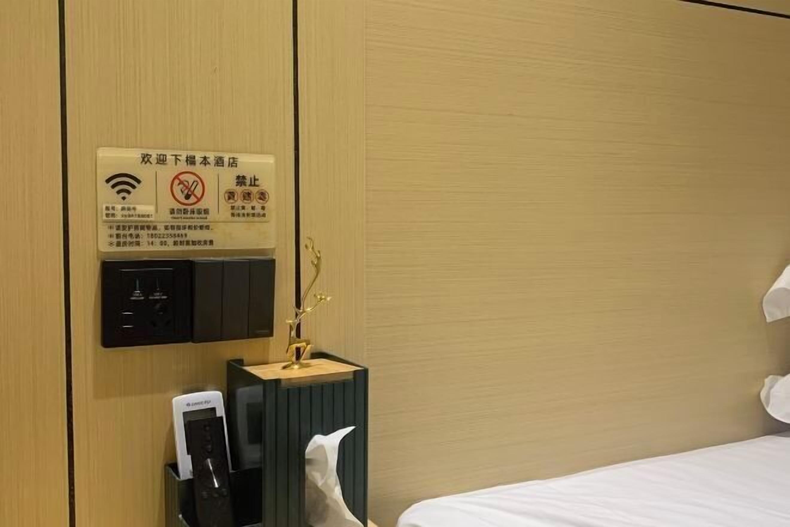 Une chambre d’hôtel comprenant un lit, une table de chevet avec une lampe, un panneau de commande fixé au mur et un panneau d’affichage contenant des informations sur l’hôtel.