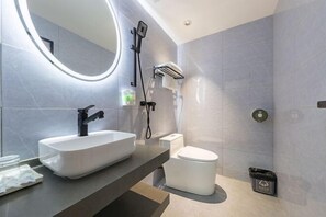 A modern bathroom with a large oval mirror, a white sink, a toilet, and a shower area. - Xinyi Hotel (Guangzhou)