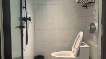 Un baño moderno con inodoro blanco, cabina de ducha de vidrio y toallero negro.