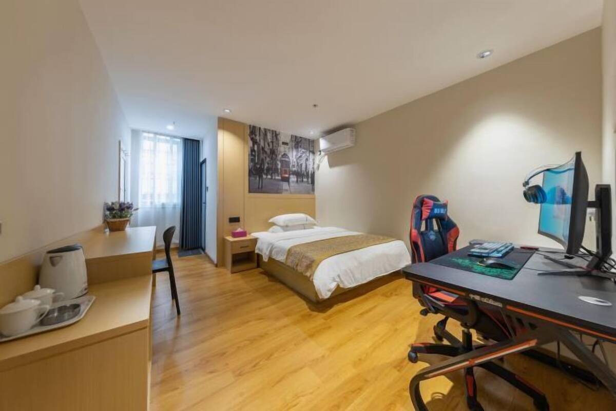 A hotel room with a bed, desk, chair, computer, and a window.