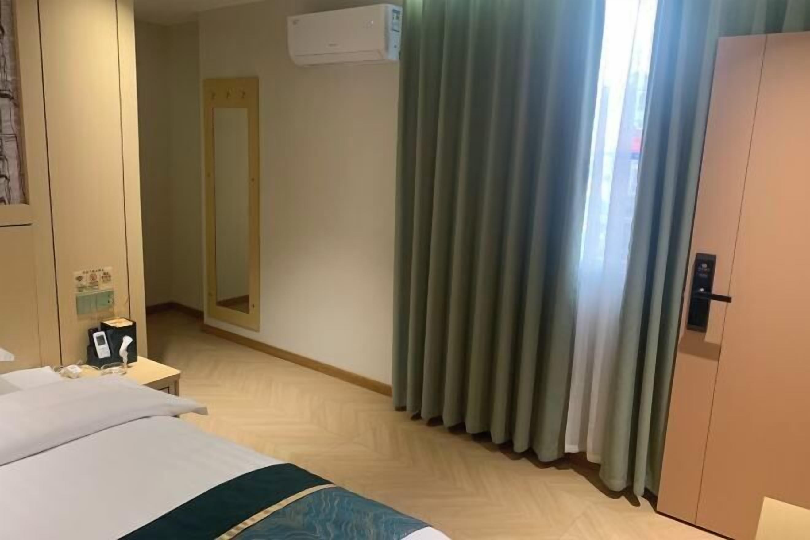 Quarto de hotel com cama, mesa de cabeceira com telefone e luminária, espelho, janela com cortinas e aparelho de ar condicionado.