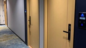 Un couloir doté d’un sol recouvert de moquette, deux portes fermées et un écran numérique sur le mur de droite.