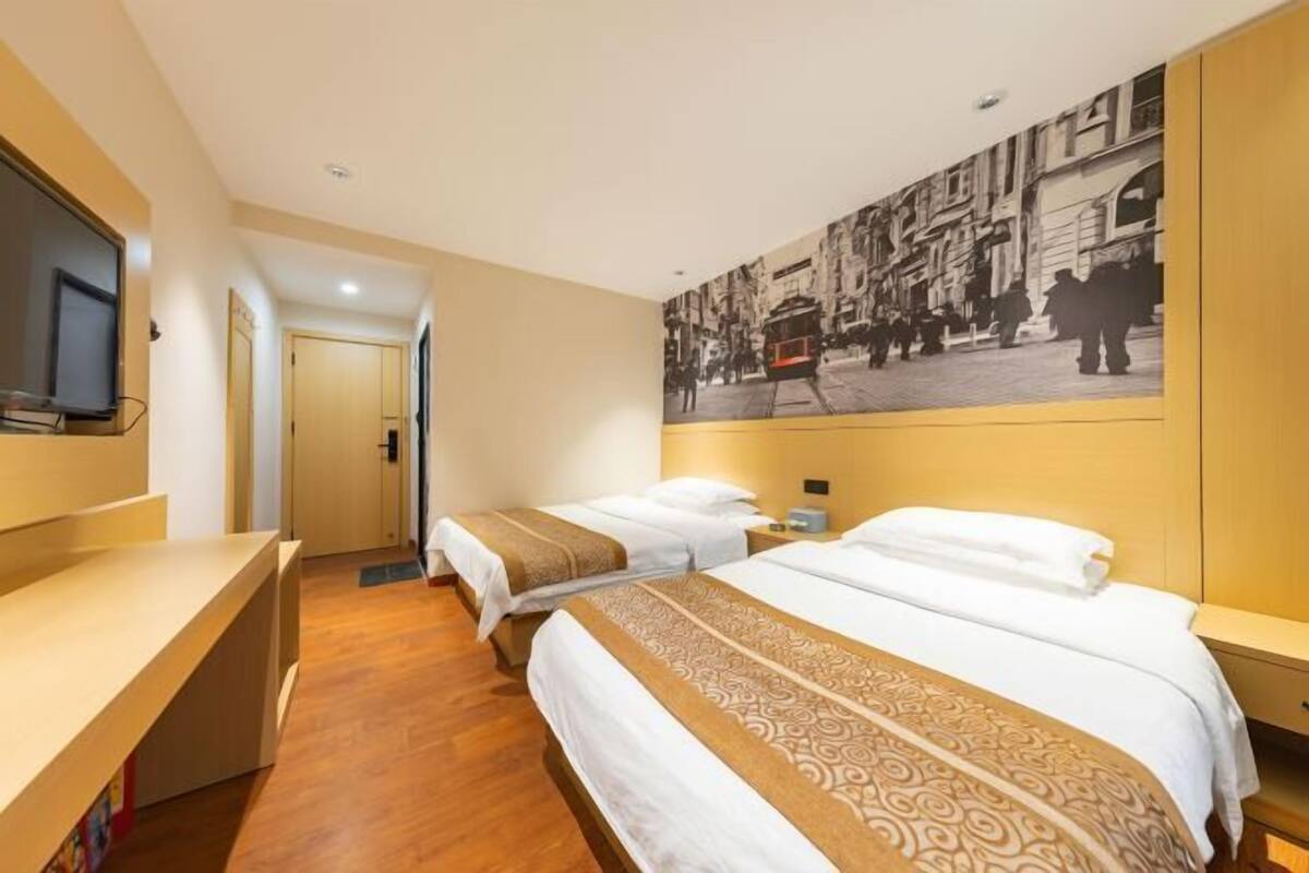 A hotel room with two beds, a desk, a television, and a large cityscape mural on the wall.