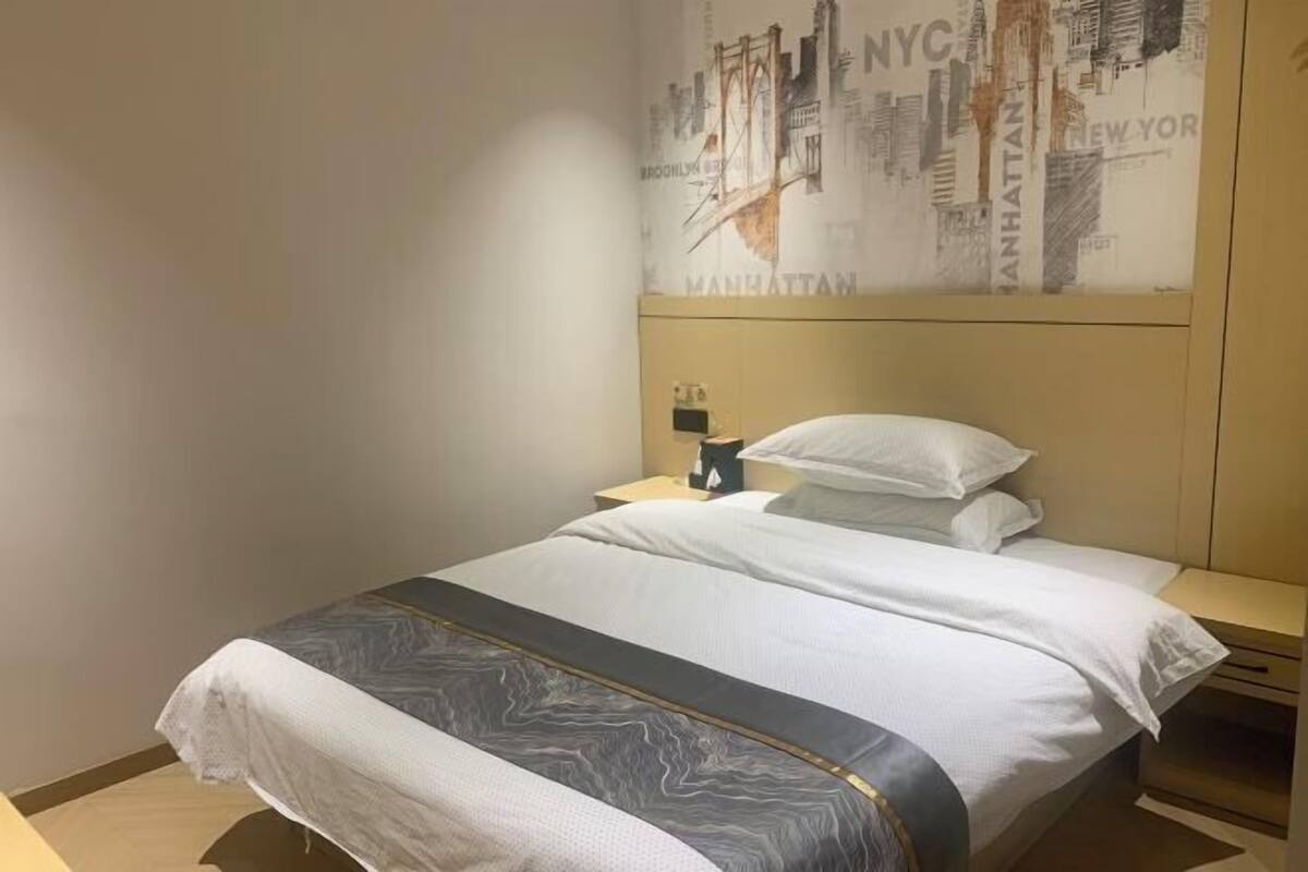 A hotel room with a bed, a nightstand, a lamp, and a wall with a cityscape poster.