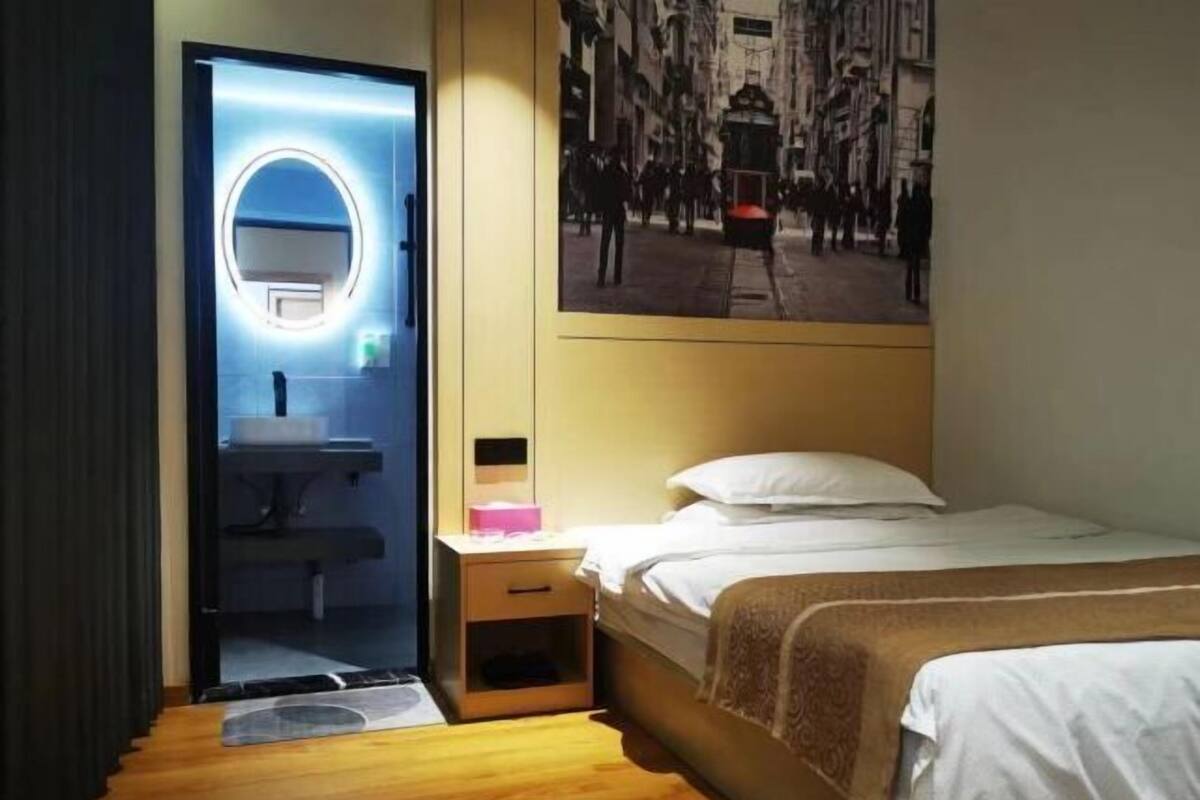 A hotel room with a bed, bedside table, and a mirror with a circular light.