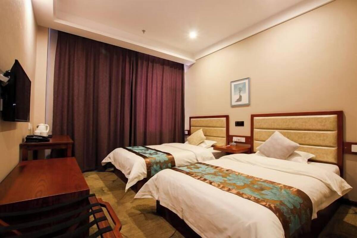 A hotel room with two beds, a desk, a chair, a television, and a large window with curtains.